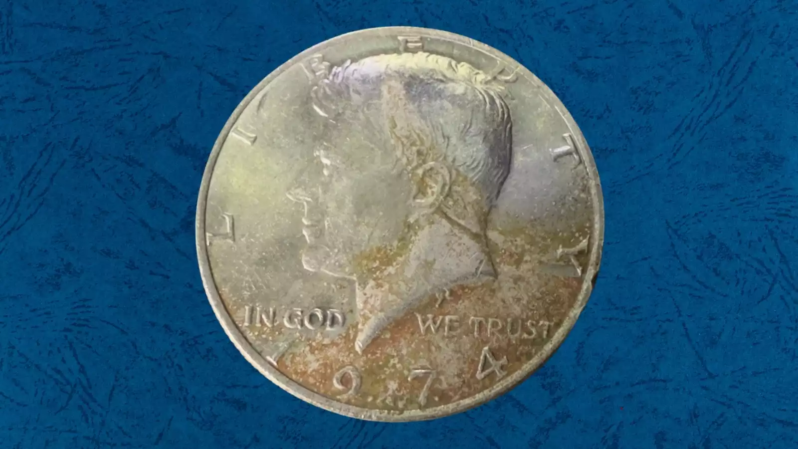 1974 Kennedy Half Dollar missing clad layer error showing reddish-orange copper exposed on coin surface where outer nickel bonding layer failed — a genuine mint error worth $50–$300+